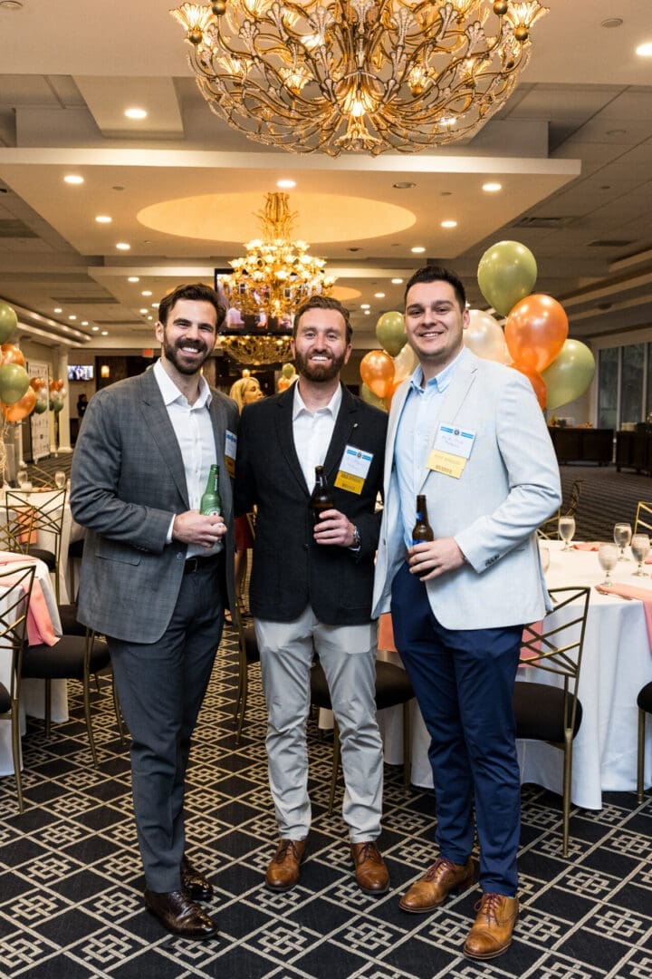 Three men in suits holding drinks at an event.