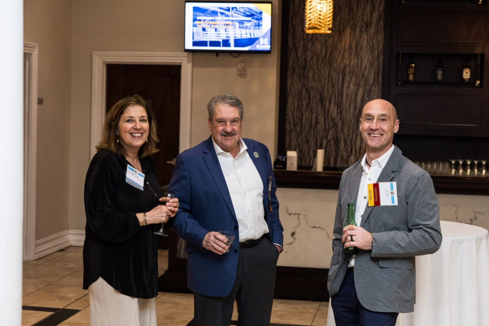 Three people are standing in a room, drinking and talking.