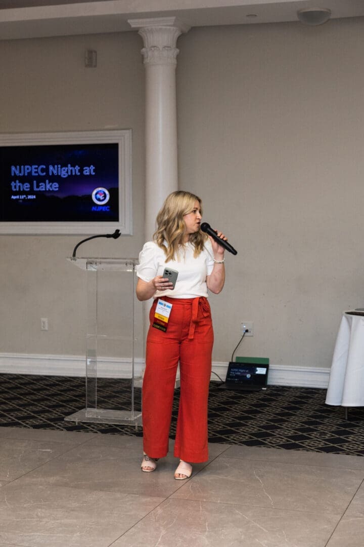 Woman in red pants speaking into microphone.