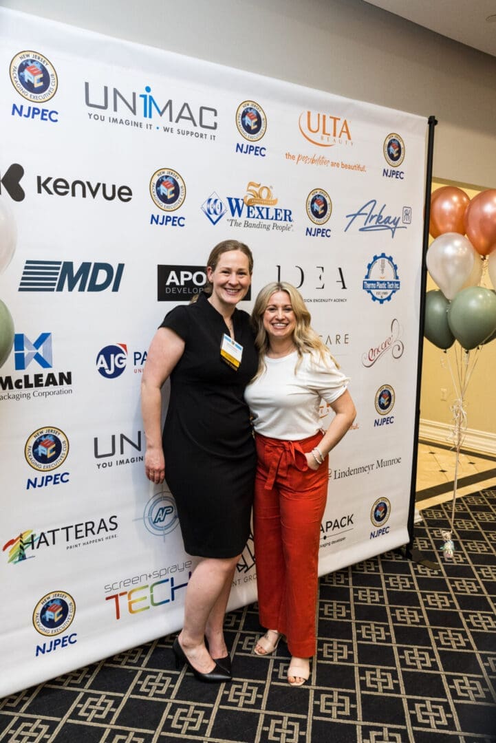 Two women posing in front of a step-and-repeat.