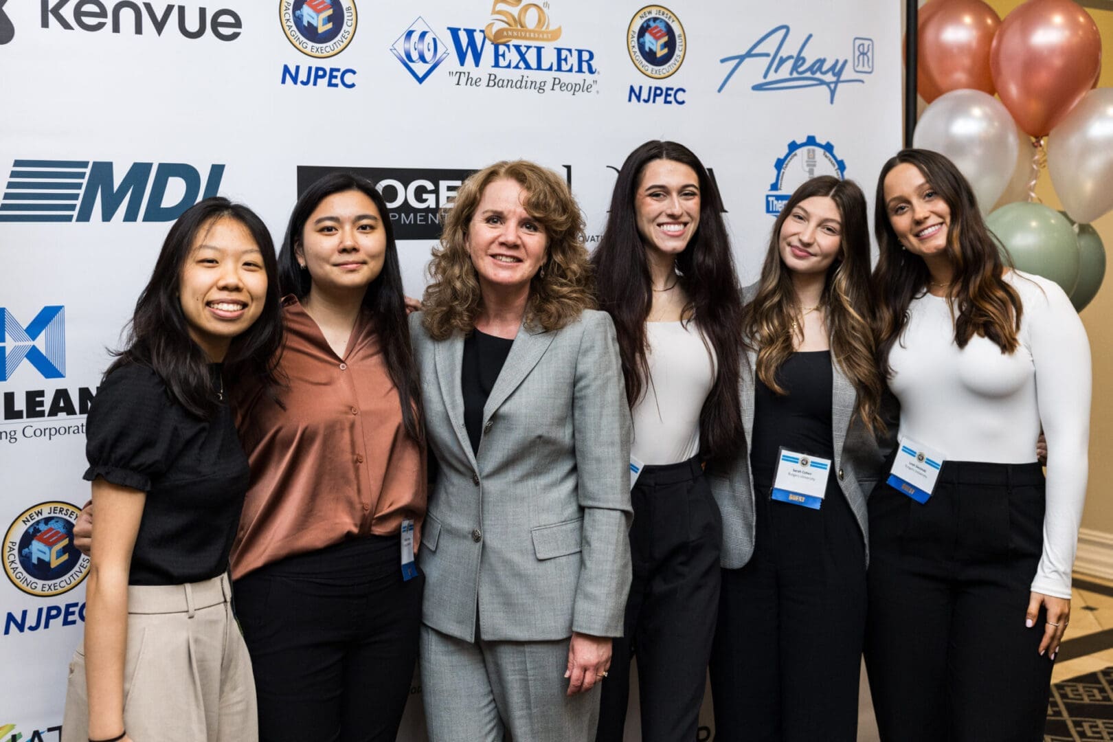 A group of six women pose for a photo at an event.