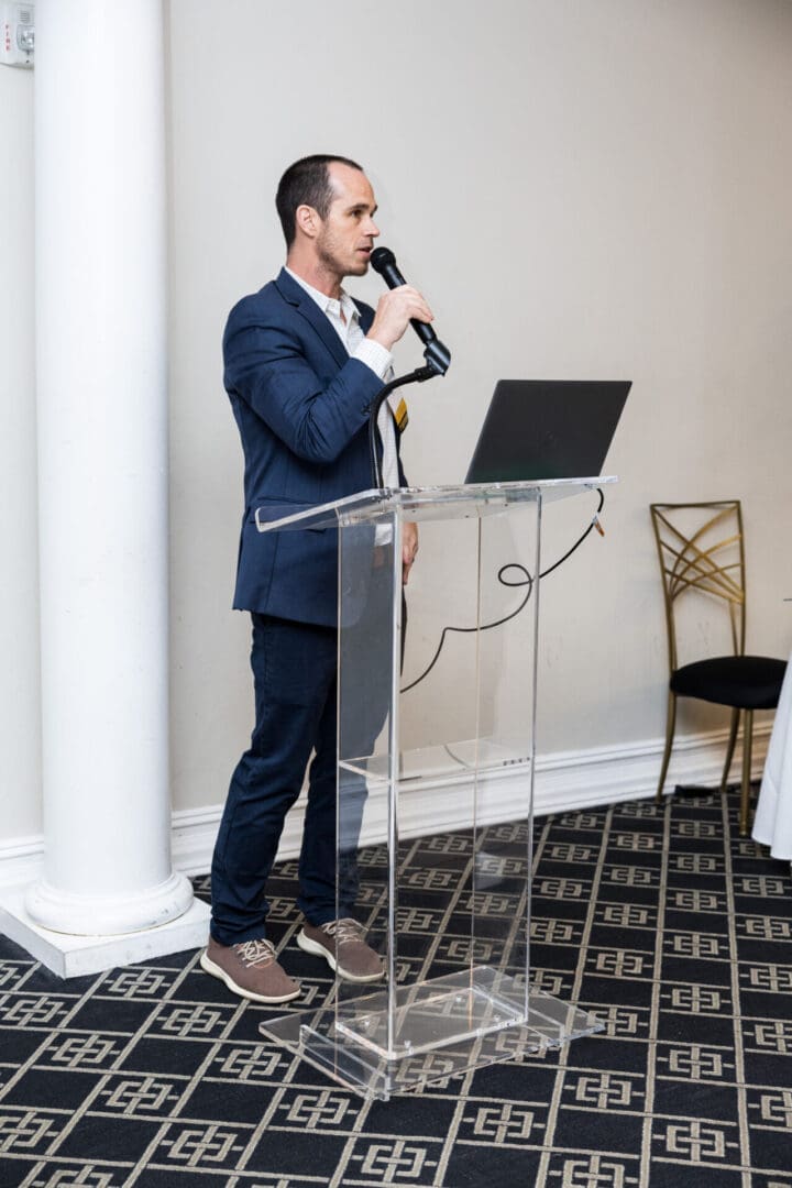 A man in a suit speaking into a microphone at a podium.