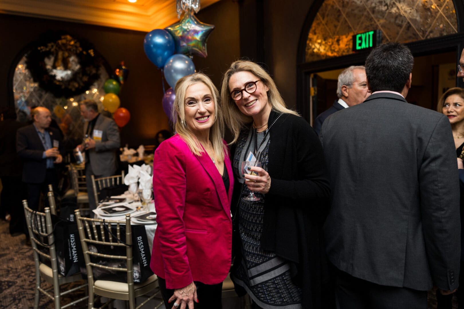 Two women smiling at a lively party.