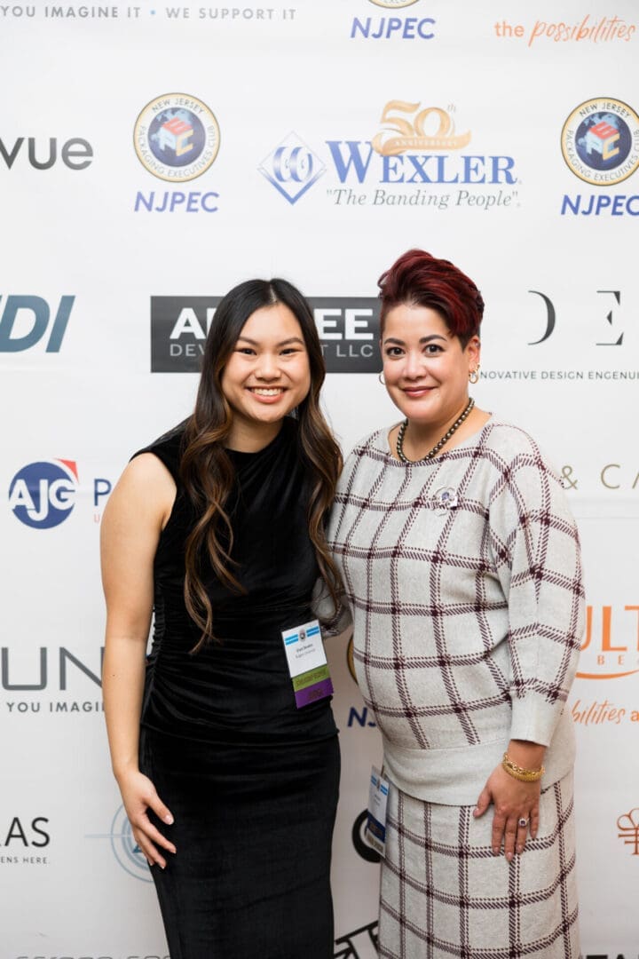 Two women posing at an event backdrop.