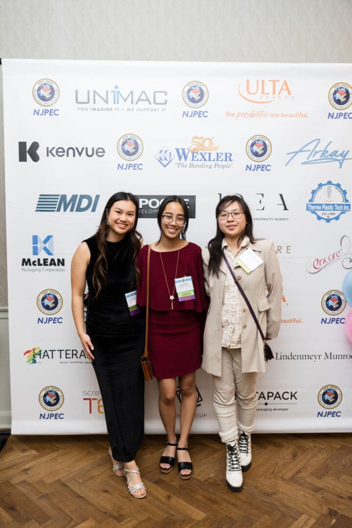 Three women posing at a conference backdrop.