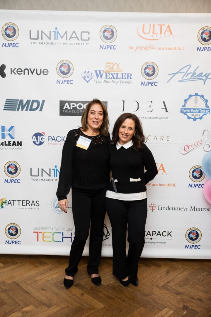 Two women posing at an event backdrop.