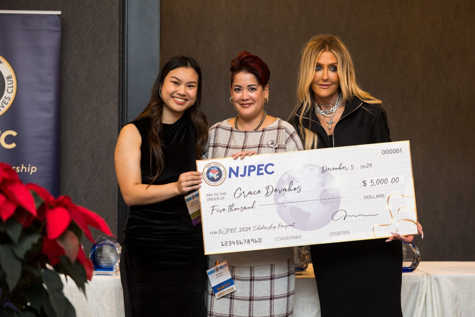 Three women holding a large scholarship check.