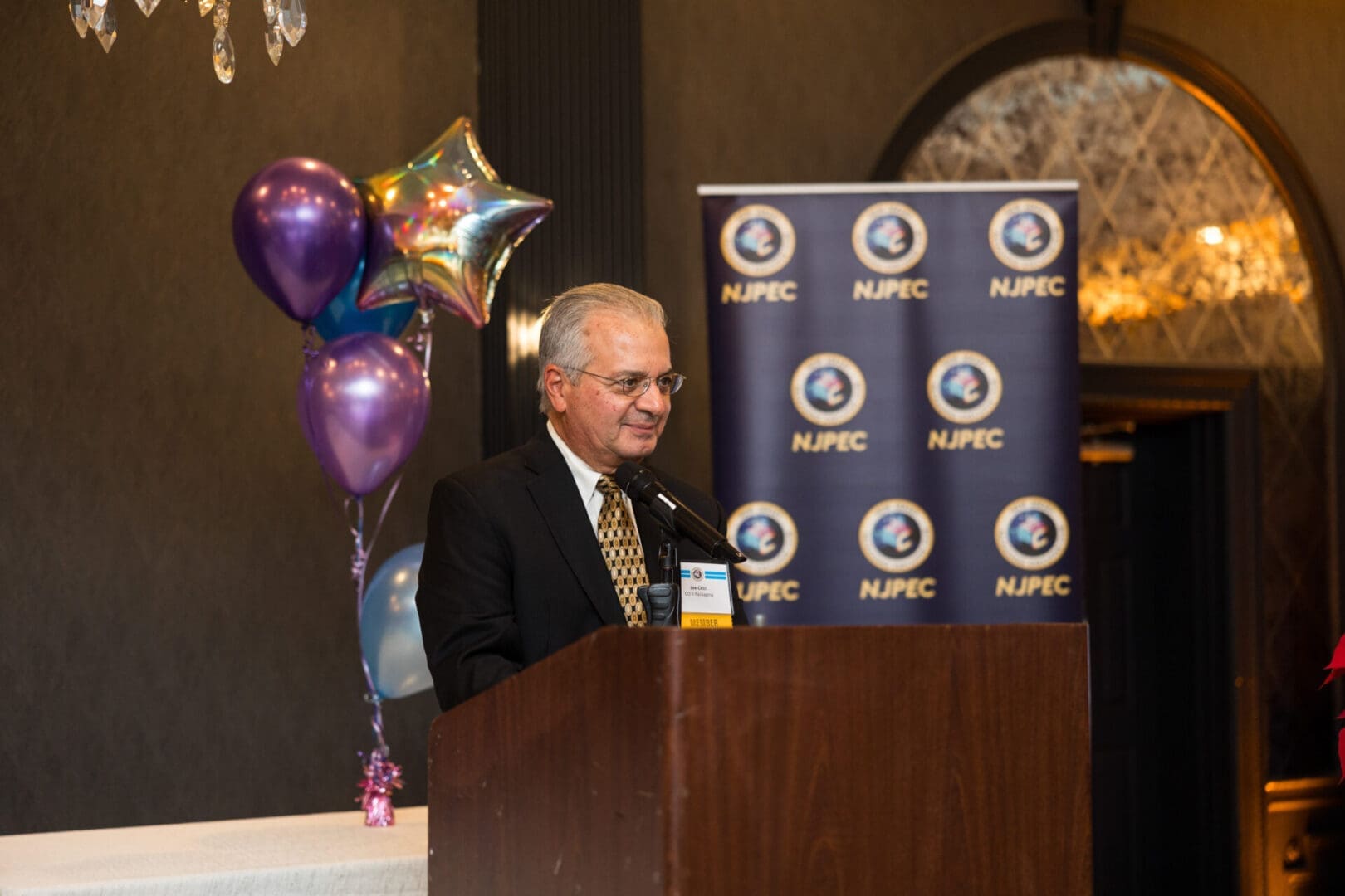 Man speaking at event with balloons.