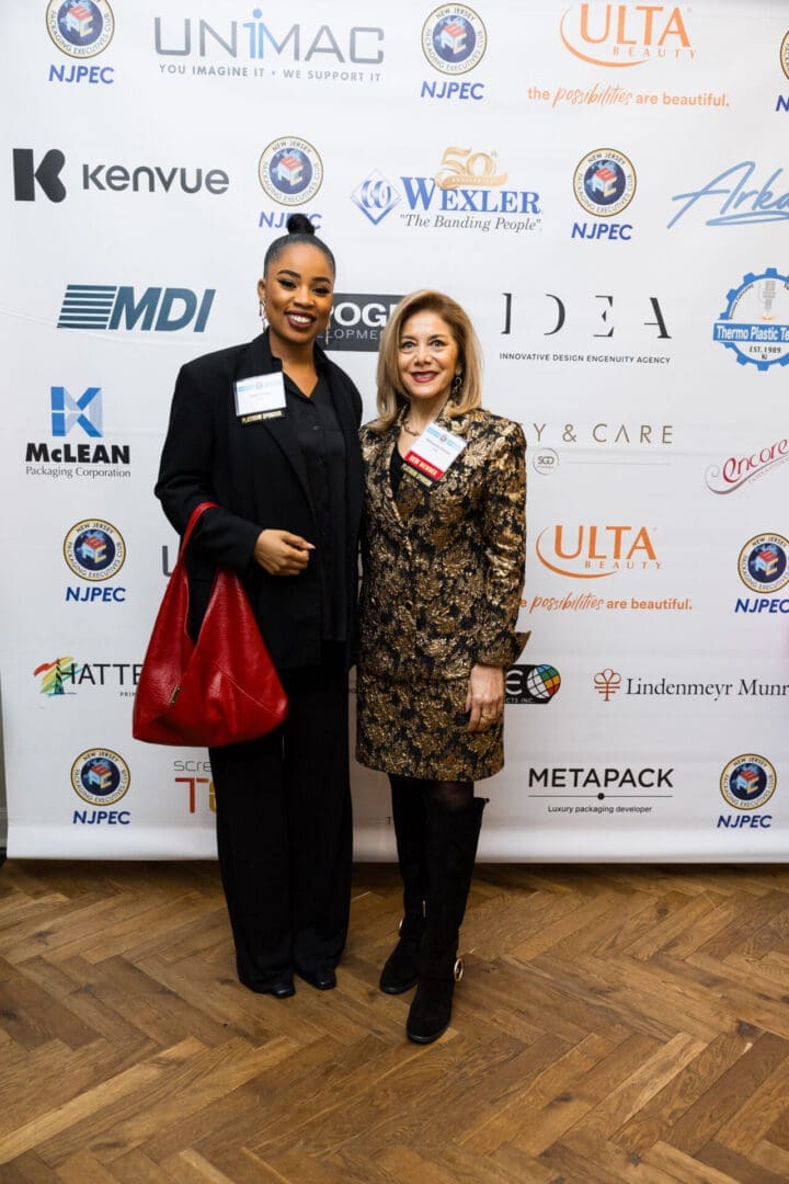 Two women posing at an event backdrop.