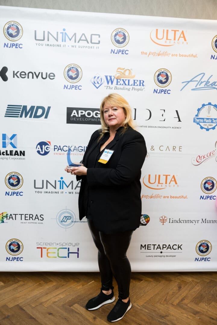 Person holding award in front of sponsor backdrop.