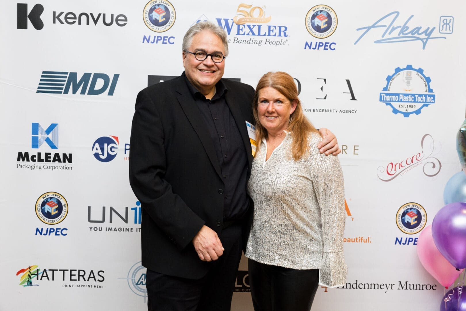 Two people posing at an event backdrop.