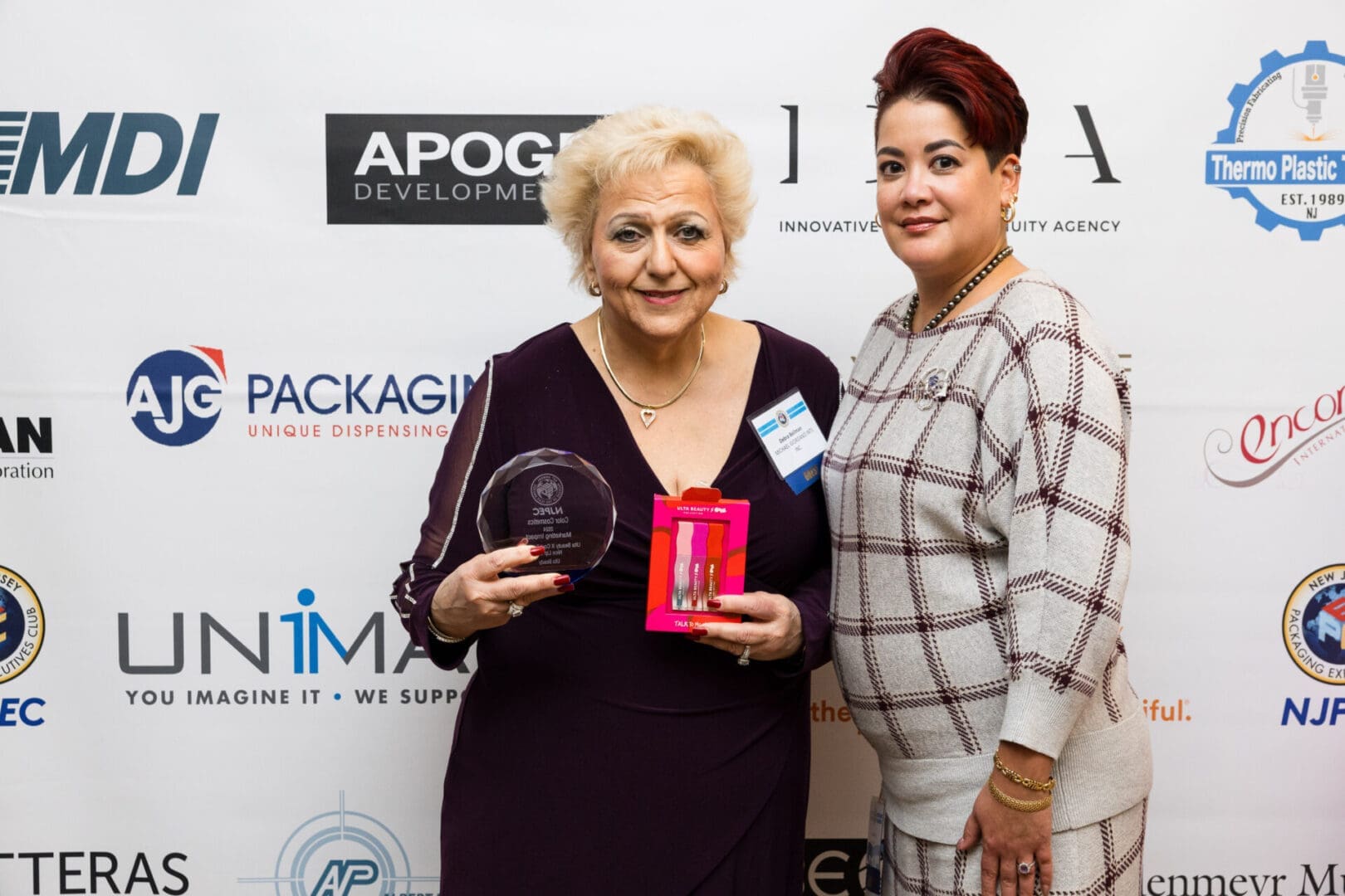 Two women posing with an award and products.