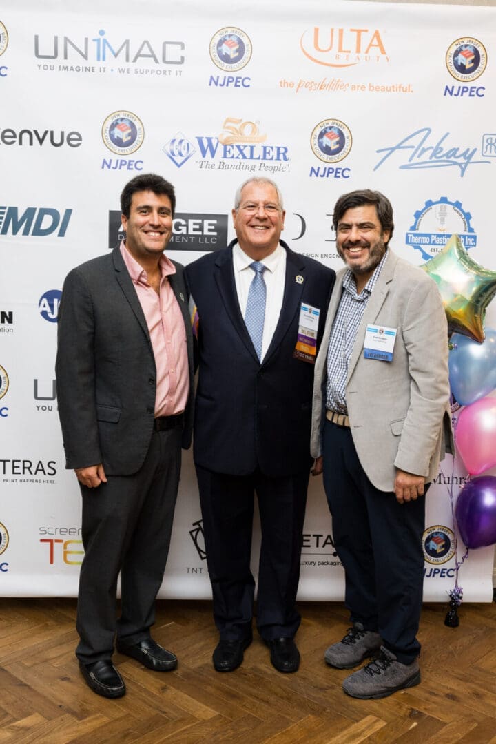 Three men posing at an event backdrop.