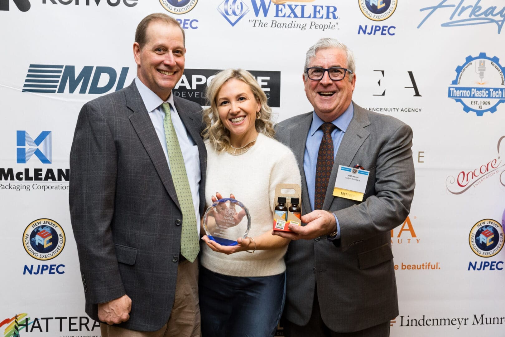 Three people holding awards and products.