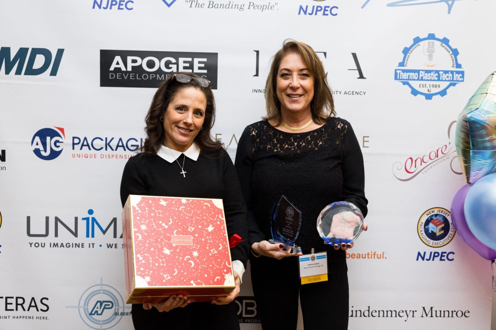 Two women holding awards and a gift box.