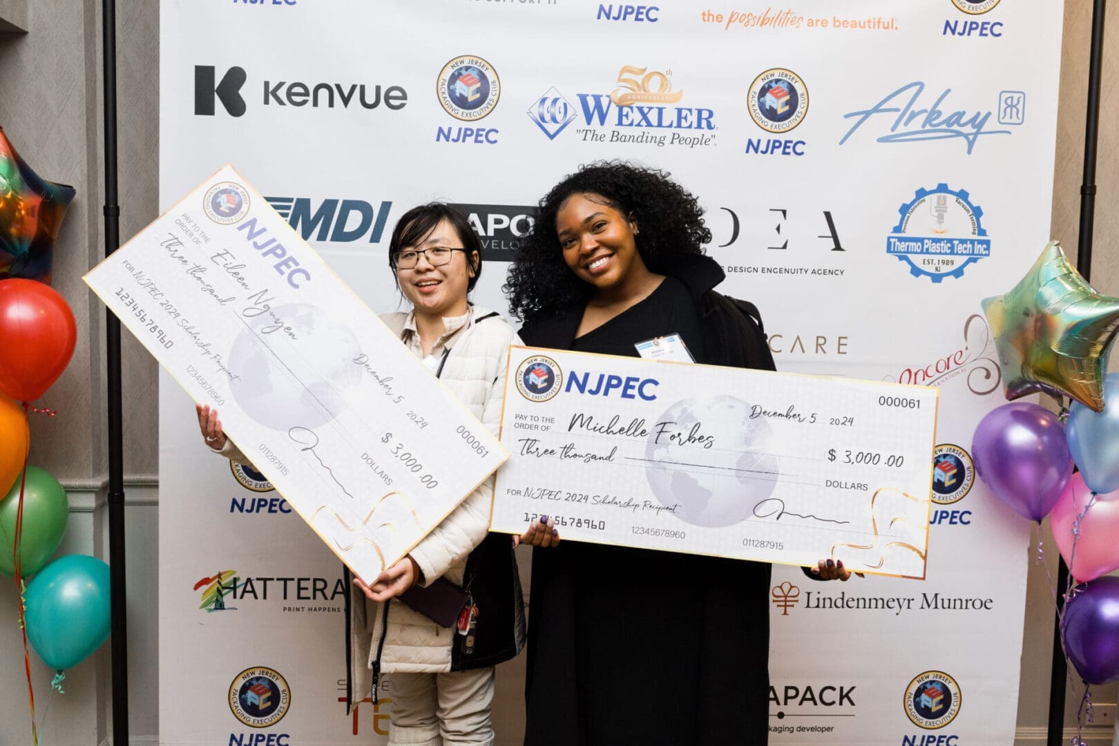 Two women holding large scholarship checks.