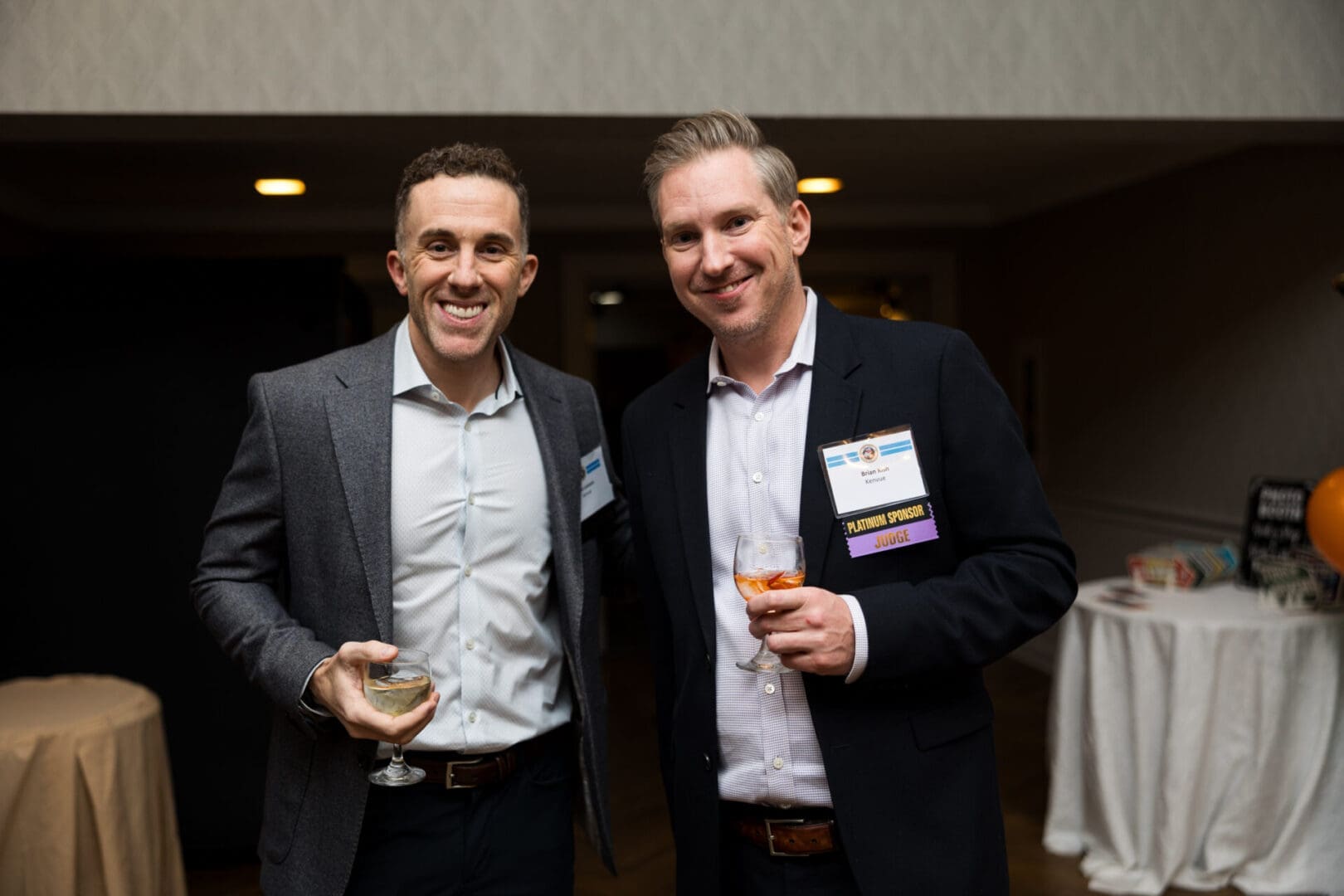 Two men smiling with drinks at event.