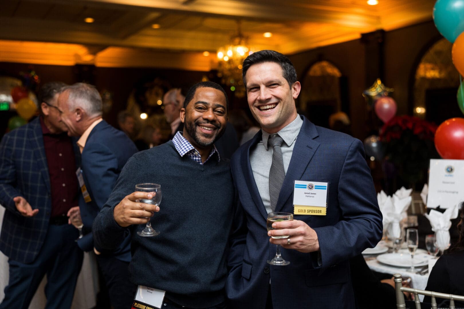 Two men smiling with drinks at event.