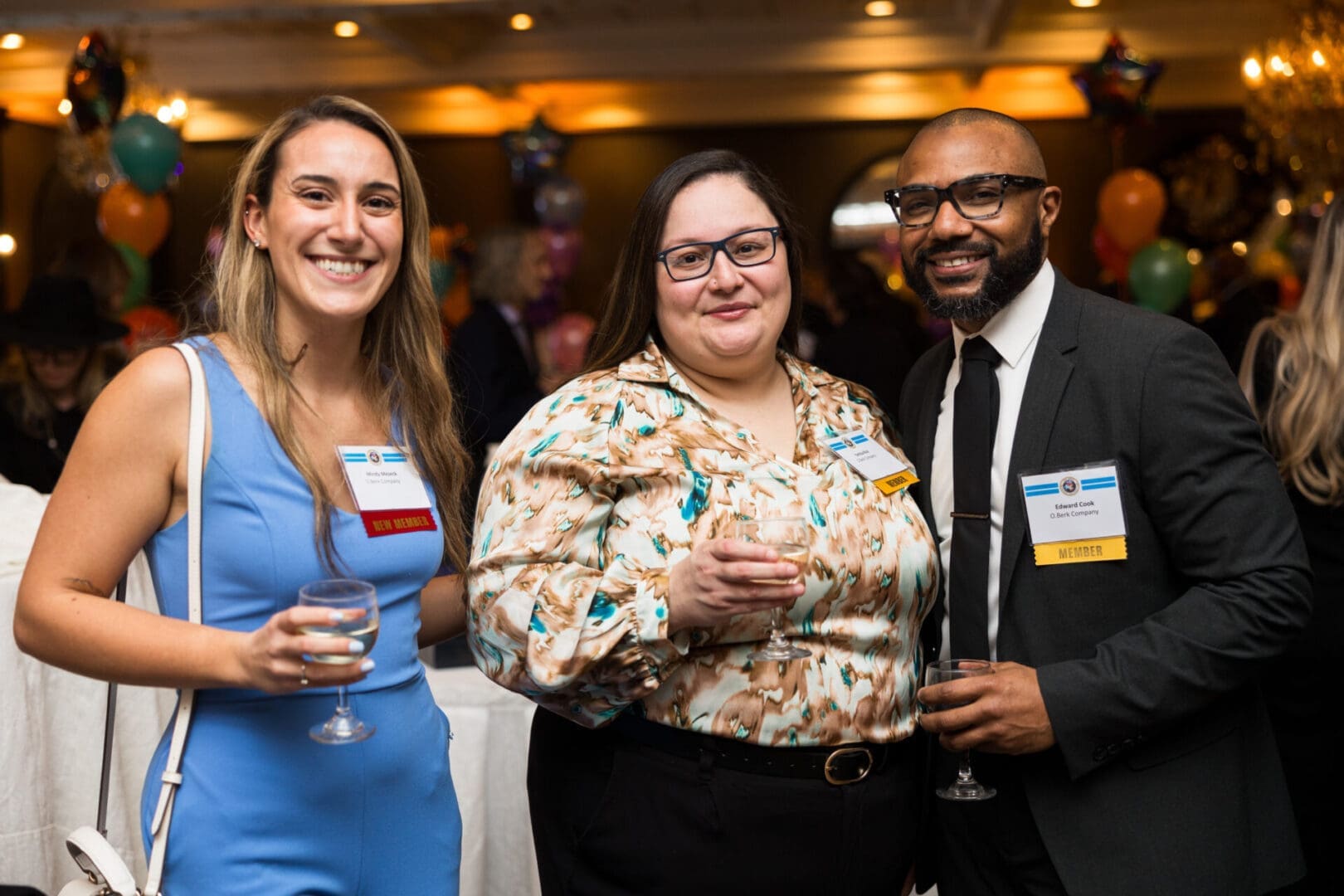 Three smiling individuals at a social gathering.