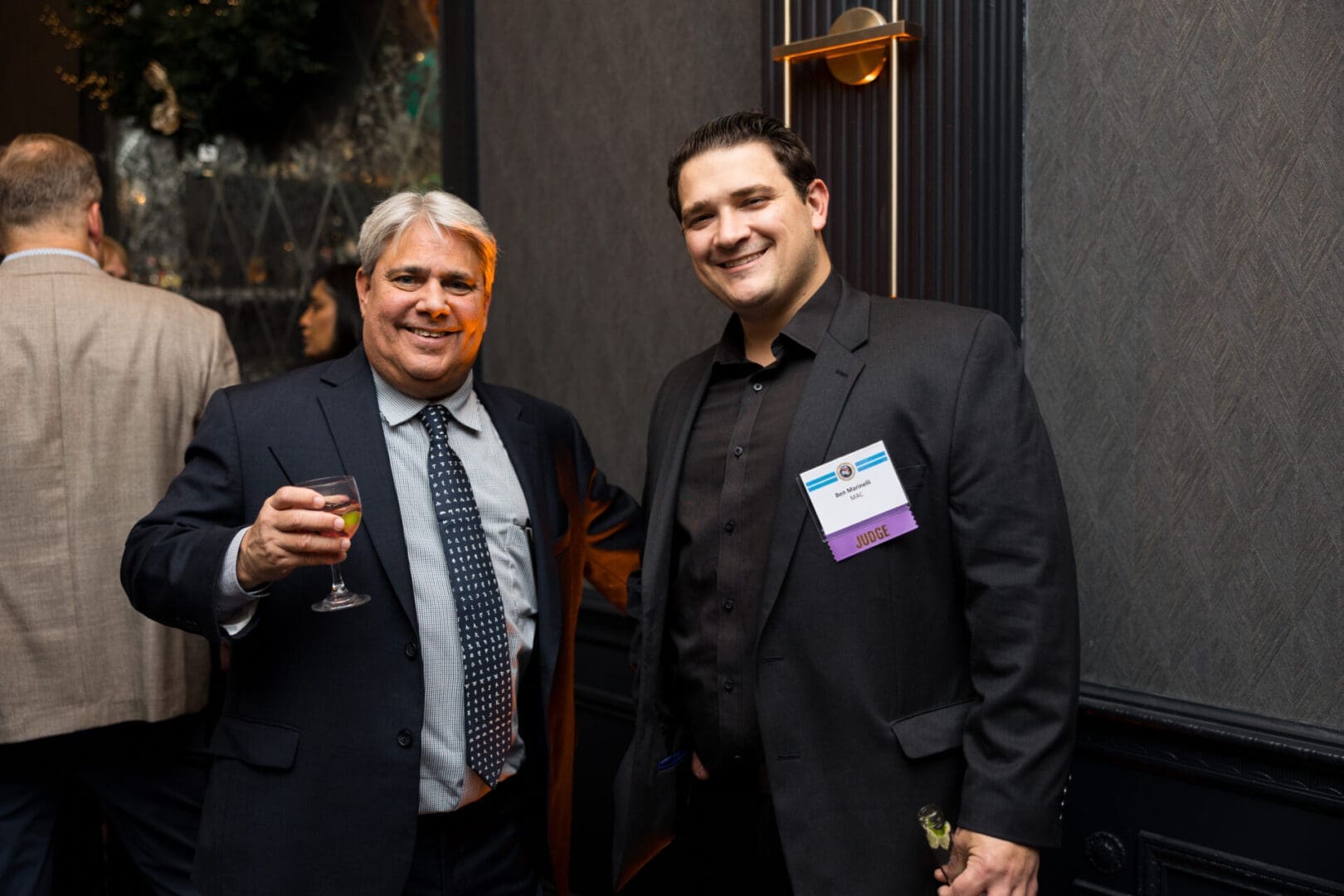 Two men posing with drinks at event.