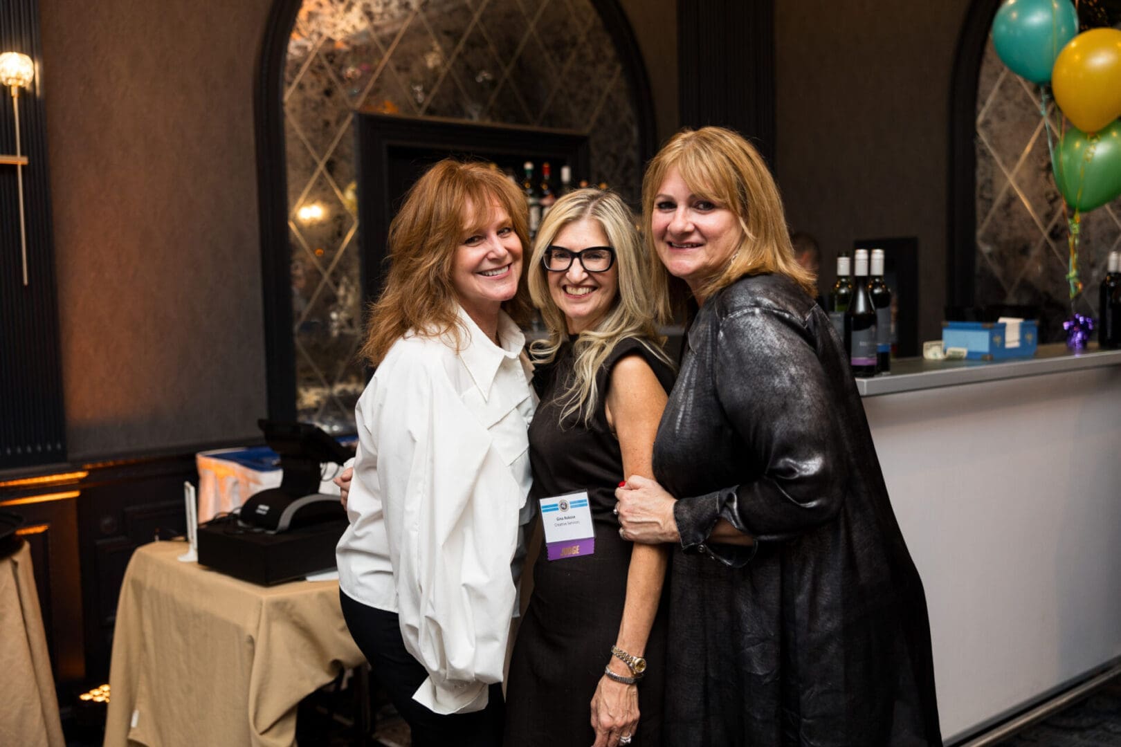 Three women smiling together at an event.