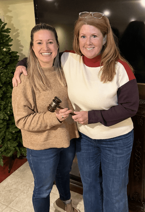 Two women smiling, holding a gavel together.