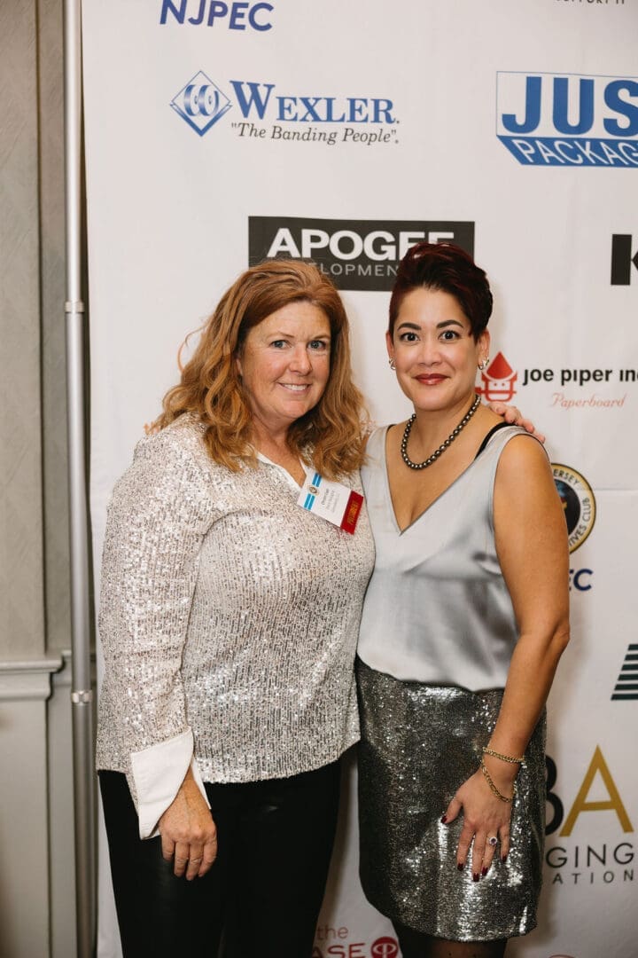 Two women posing at an event backdrop.